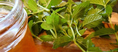 Jar of honey with fresh green mint leaves on a wooden surface.