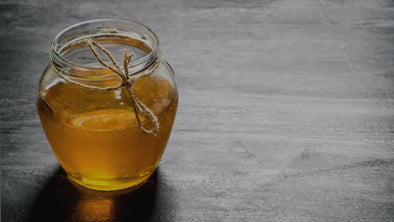 A glass jar filled with golden honey, tied with a simple twine bow, sits on a dark, rustic wooden table with copy space to the right.