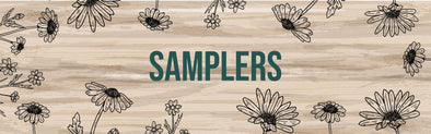A wooden background with a decorative pattern of hand-drawn daisies and small flowers in black, surrounding the word "SAMPLERS" written in bold teal letters.